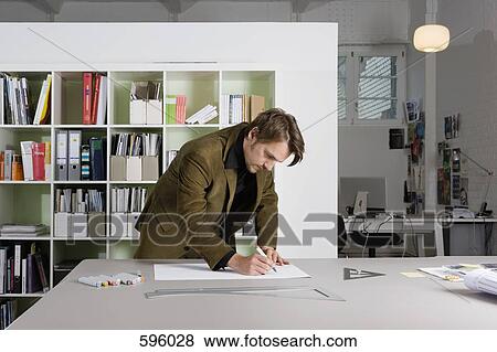 Stock Photo - A man leaning over a desk and drawing. Fotosearch