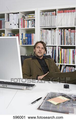 A man sitting at a desk in a design firm View Large Photo Image Stock Image - A man sitting at a desk in a design firm. Fotosearch