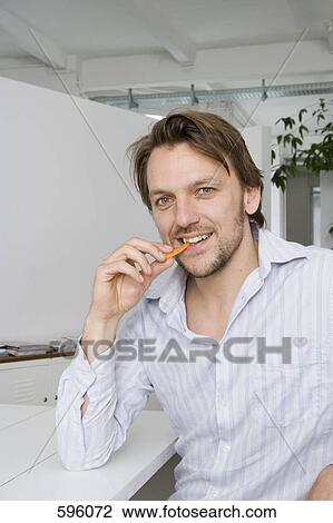 A man sitting at a table and eating a carrot stick View Large Photo Image Stock Image - A man sitting at a table and eating a carrot stick. Fotosearch