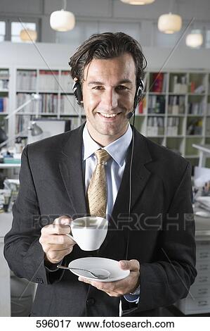 A man wearing a telephone headset and holding a cup of coffee View Large Photo Image Stock Photo - A man wearing a telephone headset and holding a cup of coffee. Fotosearch