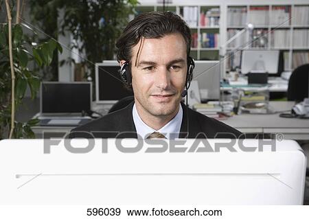 A man wearing a telephone headset and working on a computer View Large Photo Image Stock Photo - A man wearing a telephone headset and working on a computer. Fotosearch