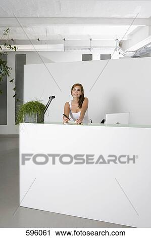 A woman behind an office reception desk with a notepad and pen View Large Photo Image Stock Image - A woman behind an office reception desk with a notepad and pen. Fotosearch