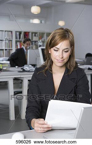 A woman looking at a document whilst sitting at a desk in an office View Large Photo Image Stock Photograph - A woman looking at a document whilst sitting at a desk in an office. Fotosearch