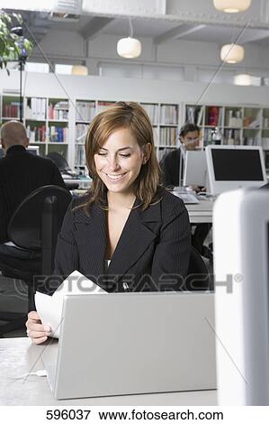 A woman sitting at a desk in an office View Large Photo Image Stock Photo - A woman sitting at a desk in an office. Fotosearch