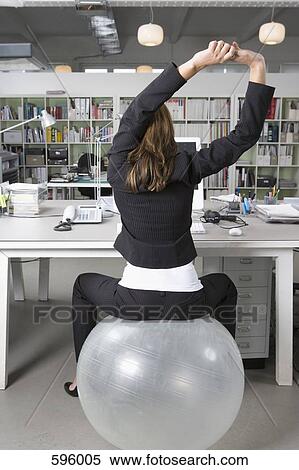 A woman sitting on an exercise ball at a desk in an office View Large Photo Image Stock Photography - A woman sitting on an exercise ball at a desk in an office. Fotosearch