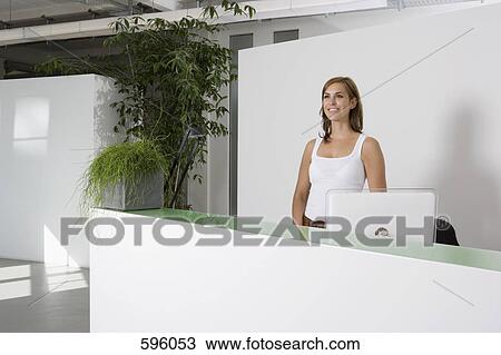 A woman standing behind an office reception desk View Large Photo Image Stock Image - A woman standing behind an office reception desk. Fotosearch