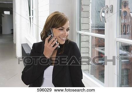 A woman standing by a window and using a mobile phone View Large Photo Image Stock Photo - A woman standing by a window and using a mobile phone. Fotosearch