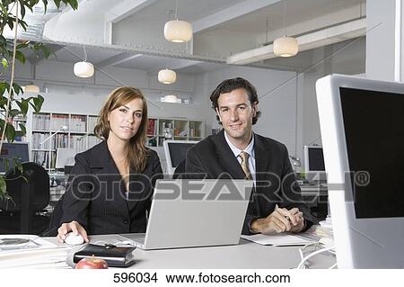 Office colleagues sitting side by side at a desk View Large Photo Image Picture - Office colleagues sitting side by side at a desk. Fotosearch