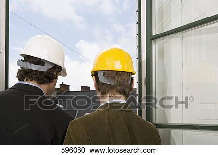 Rear view of two men standing by a window wearing hardhats View Large Photo Image Stock Image - Rear view of two men standing by a window wearing hardhats. Fotosearch