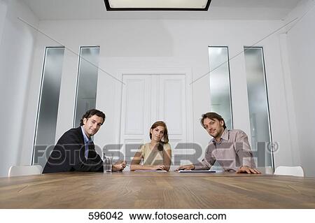 Three people sitting at a table in a conference room View Large Photo Image Stock Image - Three people sitting at a table in a conference room. Fotosearch