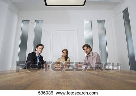 Three people sitting at a table in a conference room View Large Photo Image Stock Photograph - Three people sitting at a table in a conference room. Fotosearch