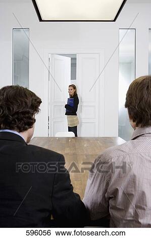 Two men seated at a table and a woman entering a conference room View Large Photo Image Stock Photograph - Two men seated at a table and a woman entering a conference room. Fotosearch