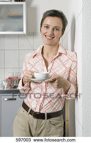 A Mature Woman leaning against a wall holding a coffee cup and saucer View Large Photo Image Stock Image - A Mature Woman leaning against a wall holding a coffee cup and saucer. Fotosearch