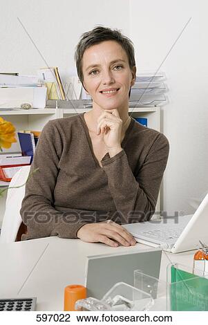 Stock Image - A mature woman sitting at office desk. Fotosearch