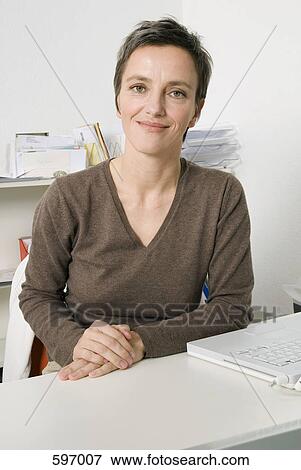 A Smiling Mature Woman sitting at a desk View Large Photo Image Stock Photo - A Smiling Mature Woman sitting at a desk. Fotosearch