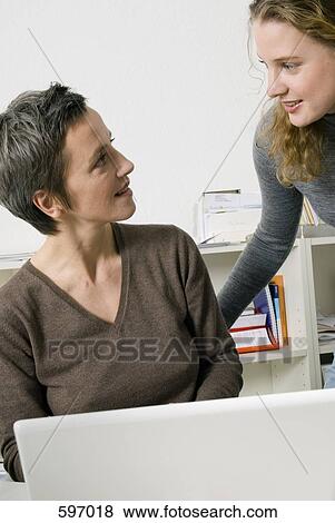 Two woman talking to each other in an office View Large Photo Image Stock Photo - Two woman talking to each other in an office. Fotosearch