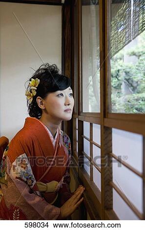 A woman wearing a kimono looking through a window View Large Photo Image Picture - A woman wearing a kimono looking through a window. Fotosearch