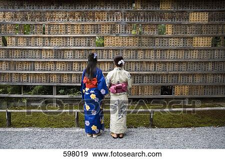 Stock Photo - Two woman wearing kimonos reading prayer blocks. Fotosearch
