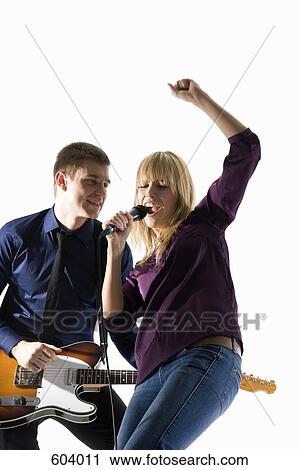 Stock Image - Studio shot of a man playing electric guitar and a woman singing into a microphone. Fotosearch