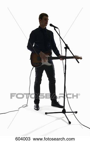 Studio shot of a man singing into a microphone and playing an electric guitar View Large Photo Image Stock Image - Studio shot of a man singing into a microphone and playing an electric guitar. Fotosearch