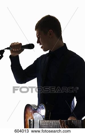 Stock Image - Studio shot of a man singing into a microphone and playing an electric guitar. Fotosearch