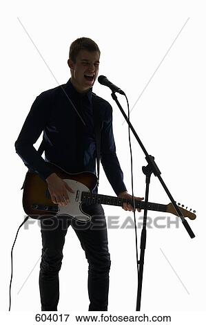 Studio shot of a man singing into a microphone and playing an electric guitar View Large Photo Image Stock Photo - Studio shot of a man singing into a microphone and playing an electric guitar. Fotosearch