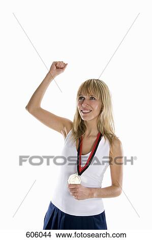 Picture - A woman holding a gold medal and raising her fist in celebration. Fotosearch