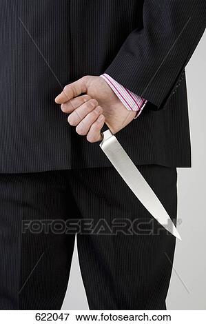 A businessman holding knife behind his back View Large Photo Image Stock Photo - A businessman holding knife behind his back. Fotosearch