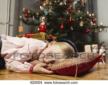 Picture - A girl sleeping next to a Christmas tree. Fotosearch