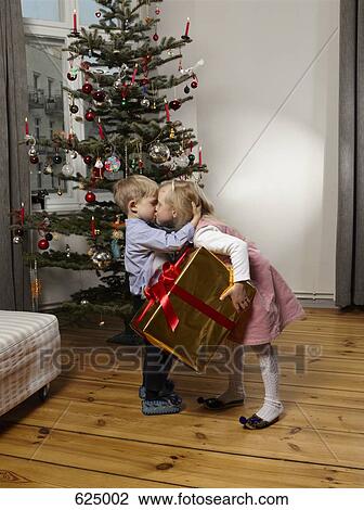 Stock Image - Brother and sister kissing in front of a Christmas tree. Fotosearch