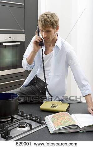 Stock Image - A man sitting on a kitchen worktop and using the telephone. Fotosearch