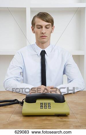 A mid adult man sitting at a table looking at a landline phone View Large Photo Image Stock Image - A mid adult man sitting at a table looking at a landline phone. Fotosearch