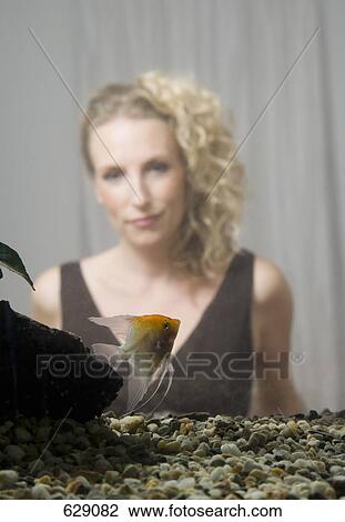 Stock Image - A mid adult woman in back of a home aquarium with a freshwater angelfish. Fotosearch