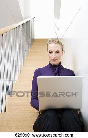 A mid adult woman sitting on a staircase using a laptop View Large Photo Image Stock Image - A mid adult woman sitting on a staircase using a laptop. Fotosearch