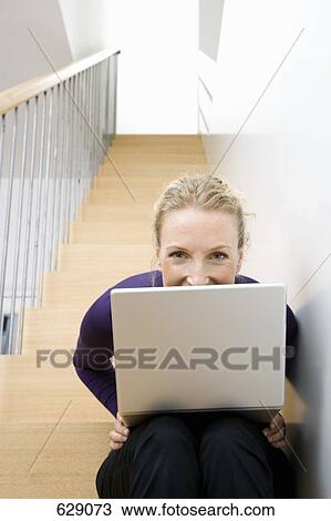 Stock Image - A mid adult woman sitting on a staircase using a laptop. Fotosearch
