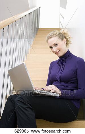 A mid adult woman sitting on a staircase using a laptop View Large Photo Image Stock Photography - A mid adult woman sitting on a staircase using a laptop. Fotosearch