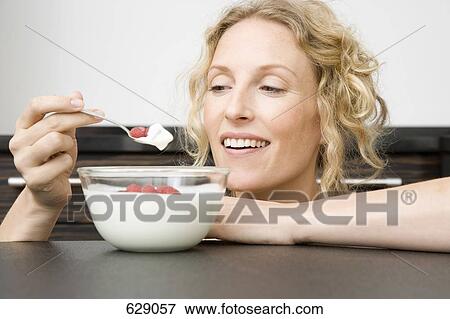 Stock Photo - A woman holding a spoon of yogurt and raspberries up to her mouth. Fotosearch