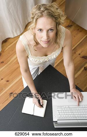 A woman writing in a notebook and using a laptop View Large Photo Image Picture - A woman writing in a notebook and using a laptop. Fotosearch