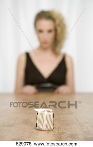A wrapped gift on a table and a woman sitting behind it View Large Photo Image Stock Photo - A wrapped gift on a table and a woman sitting behind it. Fotosearch