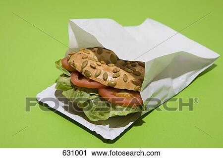 Stock Image - A Sunflower seed bagel sandwich with tomato and lettuce in a paper bag. Fotosearch