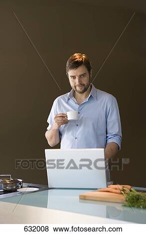 A man using a laptop and holding a coffee cup View Large Photo Image Stock Photo - A man using a laptop and holding a coffee cup. Fotosearch