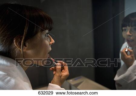 A woman applying lip gloss in a mirror View Large Photo Image Stock Photo - A woman applying lip gloss in a mirror. Fotosearch