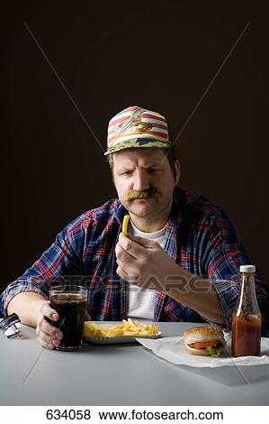 Stereotypical American man holding a french fry and staring at it View Large Photo Image Stock Photo - Stereotypical American man holding a french fry and staring at it. Fotosearch