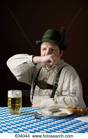 Stereotypical German man in Bavarian costume wiping mouth at a table with a beer and German meal View Large Photo Image Picture - Stereotypical German man in Bavarian costume wiping mouth at a table with a beer and German meal. Fotosearch