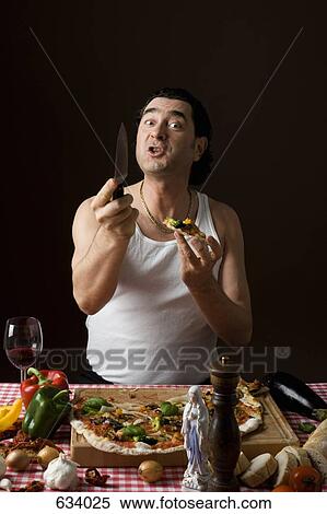 Stock Photography - Stereotypical Italian man eating pizza and holding a knife aggressively. Fotosearch