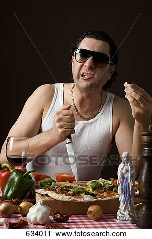 Stock Image - Stereotypical Italian Man sticking a knife in a cutting board aggressively and eating pizza. Fotosearch