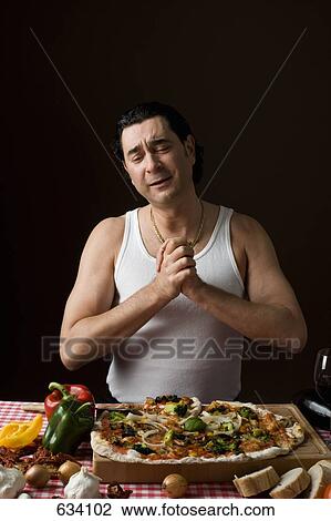 Stock Image - Stereotypical Italian man with hands clasped in gratitude looking at a pizza. Fotosearch
