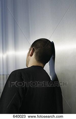 Stock Image - A man leaning against a wall. Fotosearch