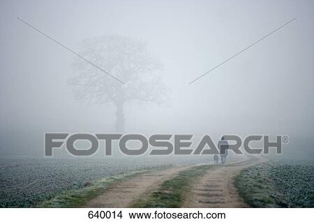 A person and dog walking along a foggy country path View Large Photo Image Picture - A person and dog walking along a foggy country path. Fotosearch