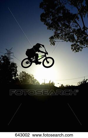 Stock Image - Silhouette of a person doing a stunt on a BMX bicycle. Fotosearch